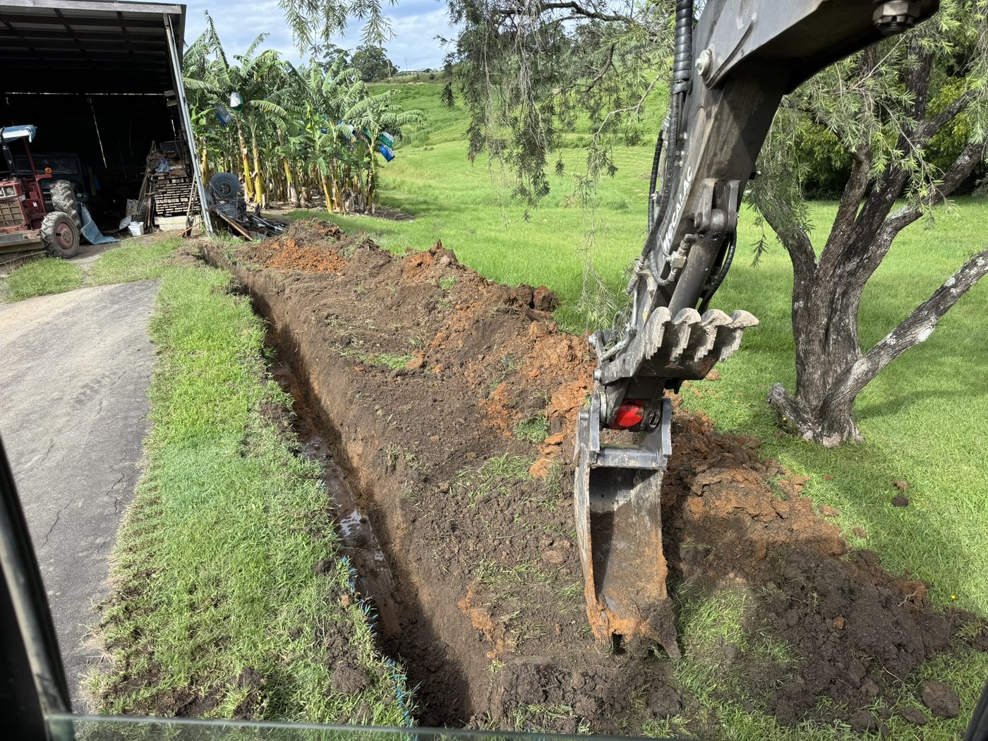 Excavator digging a drainage trench beside a farm driveway, Coramba Rd Coffs Harbour